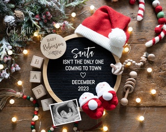 May include: A black letter board with the text "Santa isn't the only one coming to town" and "December 2023". A wooden circle with the text "Baby Robinson" is on the left side of the board. A small ultrasound image is on the right side of the board. There are Christmas decorations around the board, including a Santa hat, a candy cane, and a string of lights.