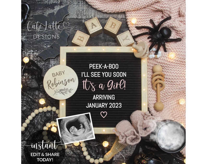 May include: A black letter board with the text "Peek-a-boo I'll see you soon It's a girl! Arriving January 2023" surrounded by a variety of baby-themed items, including a wooden sign that says "Baby Robinson", a black spider, a wooden rattle, and a pair of pink booties.
