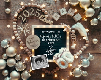 May include: A black letter board with the text "IN 2025 WE'LL BE Popping Bottles OF A DIFFERENT KIND!" and the date "JANUARY 2025". A wooden circle with the text "BABY Robinson" is on the left side of the board. A small ultrasound image is on the bottom left of the board. A pair of white knitted baby booties are on the bottom right of the board. The board is surrounded by wooden beads, gold ornaments, and a string of lights.