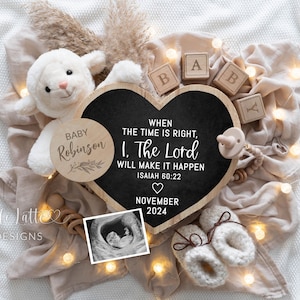 Puede incluir: Un pizarrón de madera en forma de corazón con el texto "WHEN THE TIME IS RIGHT, 1. THE LORD WILL MAKE IT HAPPEN ISAIAH 60:22" y "NOVEMBER 2024". También hay un círculo de madera con el texto "BABY Robinson" y un pequeño peluche de cordero blanco en la imagen.