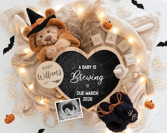 Puede incluir: Anuncio de embarazo con temática de Halloween con un osito de peluche con sombrero de bruja, una pizarra en forma de corazón con el texto "A Baby is Brewing" y una ecografía. La fecha prevista de parto es marzo de 2026.