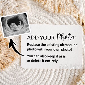 May include: A white card with black text that reads "ADD YOUR Photo" and "Replace the existing ultrasound photo with your own photo! You can also keep it as is or delete it entirely." The card also has the text "Cafe Latte DESIGNS" in black text. The card is sitting on a woven straw mat with a white fringe.