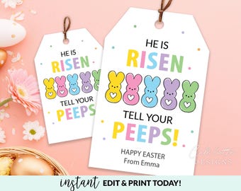 Könnte beinhalten: Zwei weiße Oster-Geschenkanhänger mit dem Text "He is Risen" und "Tell Your Peeps!" in bunten Buchstaben. Jeder Anhänger zeigt eine Reihe von Cartoon-Hasenfiguren in Gelb, Rosa, Blau, Lila und Grün. Die Anhänger haben eine braune Schnur zum Aufhängen.