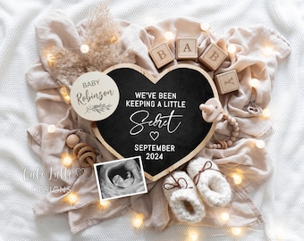Könnte beinhalten: Ein herzförmiges Schild aus Schiefer mit dem Text "We've been keeping a little secret" und dem Datum "September 2024". Das Schild ist umgeben von Babyschuhen, einer Holzrassel, einem Schnuller und einem Holzkreis mit dem Text "Baby Robinson".