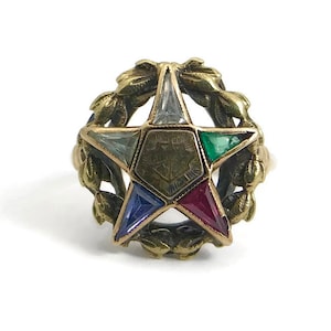 May include: A gold ring with a five-pointed star set with colorful gemstones. The star is surrounded by a wreath of leaves.