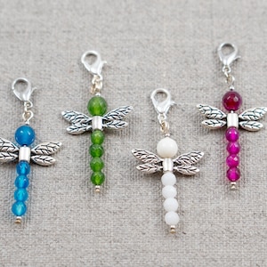 May include: Four dragonfly charms with different colored beads. The charms are made of silver metal and have a beaded chain with a lobster clasp. The beads are green, white, blue, and pink.