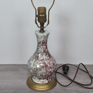 May include: A table lamp with a bulbous, fluted ceramic base featuring a mottled pattern of maroon and pale green. The lamp includes a brass-colored metal base, a brass socket assembly with a harp, and a brown electrical cord with a black plug.