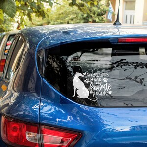 Peut inclure: Une voiture bleue avec un autocollant en vinyle blanc sur la vitre arri&egrave;re. L'autocollant repr&eacute;sente une silhouette de l&eacute;vrier et le texte "Les l&eacute;vriers sont mes personnes pr&eacute;f&eacute;r&eacute;es".