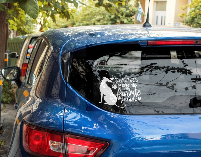 Peut inclure: Une voiture bleue avec un autocollant en vinyle blanc sur la vitre arri&egrave;re. L'autocollant repr&eacute;sente une silhouette de l&eacute;vrier et le texte "Les l&eacute;vriers sont mes personnes pr&eacute;f&eacute;r&eacute;es".