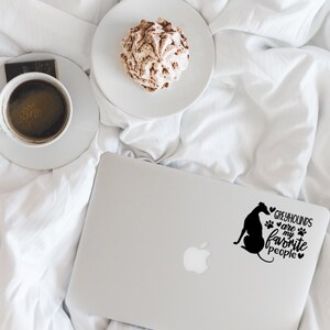 Peut inclure: Un ordinateur portable blanc avec une silhouette noire de l&eacute;vrier et le texte "Les l&eacute;vriers sont mes personnes pr&eacute;f&eacute;r&eacute;es" avec des empreintes de pattes et des c&oelig;urs. L'ordinateur portable est sur un couvre-lit blanc avec une tasse de caf&eacute; et une p&acirc;tisserie.