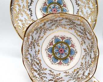 Könnte beinhalten: Ein Vintage-Teetassen- und Untertassen-Set mit einem zarten blauen und goldenen Blumenmuster. Die Untertasse hat einen gewellten Rand und einen goldenen Rand.