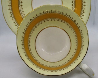 May include: A yellow and white teacup and saucer set with a gold trim and intricate pattern. The saucer has a wide yellow band with a gold trim and a delicate pattern.