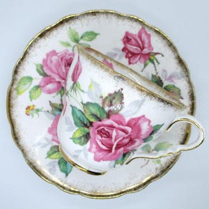 Puede incluir: Juego de taza y platillo de té blanco con un diseño de rosas rosas y hojas verdes. Los bordes están adornados con dorado. Un conjunto elegante para el té.