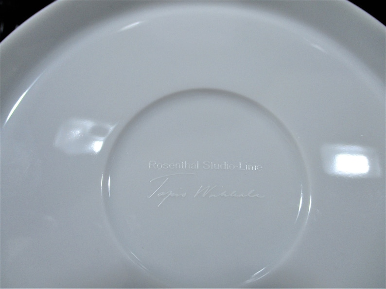 以下が含まれることがあります： 白のセラミックソーサーで、中央がくぼんでいます。「Rosenthal Studio Linie」と「Topio Miracle」の文字が表面にさりげなくエンボス加工されています。ソーサーは滑らかで光沢のある仕上がりです。