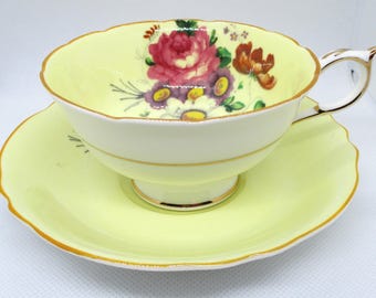 Può includere: Un set da tè giallo con un motivo floreale. La tazza e il piattino hanno un bordo ondulato e un bordo dorato.