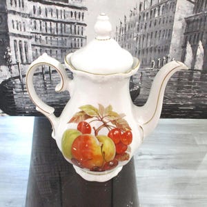 Puede incluir: Tetera de porcelana blanca con ribete dorado y diseño de frutas. El diseño presenta cerezas, manzanas y peras.