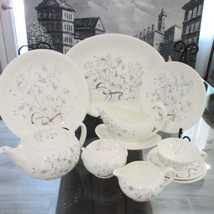 Könnte beinhalten: Ein weißes Teeservice mit silbernem Blumendesign. Das Set beinhaltet eine Teekanne, eine Zuckerdose, eine Milchkännchen, zwei Teller, eine Sauciere und eine Tasse mit Untertasse.