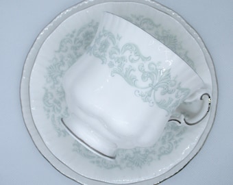 May include: A white teacup and saucer set with a delicate green floral pattern. The cup has a rounded shape and a handle. The saucer has a scalloped edge.