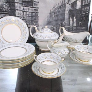 Puede incluir: Un juego de té completo de porcelana blanca con ribete dorado y un delicado estampado floral. El juego incluye platos, tazas, platillos, una tetera, una crema y una salsera.