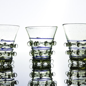 Peut inclure: Trois verres en verre transparent avec une teinte vert clair, présentant une surface texturée avec de petits picots en verre et des fils de verre bleus horizontaux enroulés autour des sections médiane et inférieure de chaque récipient.