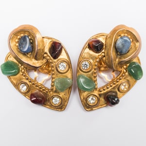 Könnte beinhalten: Ein Paar goldfarbene Ohrringe mit herzförmigem Design. Jeder Ohrring verfügt über eine Vielzahl farbiger Edelsteine, darunter Blau, Grün und Rot, und ist mit kleinen, klaren Kristallen akzentuiert. Die Ohrringe haben eine Vintage- oder Antik-Ästhetik.