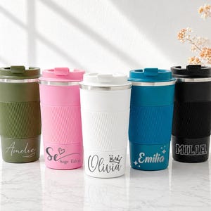 May include: Five personalised travel mugs in olive green, pink, white, teal, and black. Each mug has a ribbed silicone sleeve and a stainless steel lid. Names are printed on the front of each mug in a script font.