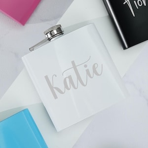 Könnte beinhalten: Fünf personalisierte Flachmänner in verschiedenen Farben. Die Flachmänner sind aus Metall und haben einen silbernen Verschluss. Die Namen "Jasmine", "Fiorella", "Katie", "Hadiya" und "Morales" sind auf die Flachmänner graviert.