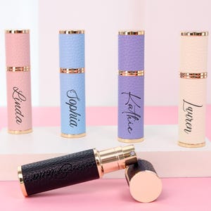 May include: A collection of refillable perfume atomizers in various pastel colors, including pink, blue, and lavender. Each atomizer has a gold-colored top and bottom, with a textured leather-like finish. Names are printed on the atomizers.