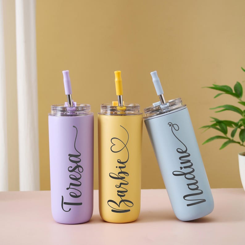 May include: Three personalized stainless steel tumblers in pastel colors: lavender, yellow, and light blue. Each tumbler has a matching straw and lid, with a name in a cursive font. The names are Teresa, Barbie, and Nadine.