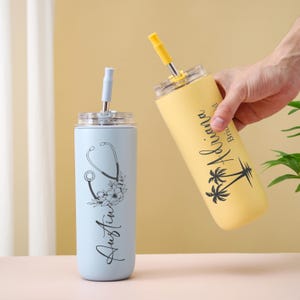 May include: Two stainless steel tumblers with straws. One is light blue with a stethoscope and floral design, the name "Austin" is written vertically. The other is yellow with the name "Ariana" and palm trees.