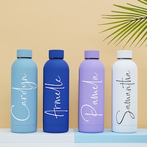 May include: Four personalized water bottles in blue, purple, white, and blue. The bottles are lined up on a light blue surface. The names "Carolyn", "Armelle", "Pamela", and "Samantha" are written in white on the bottles.