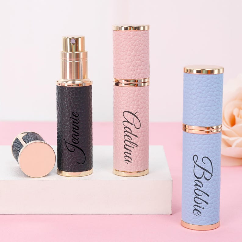 May include: A collection of three refillable perfume atomizers in black, pink, and blue, with gold-colored accents. The black atomizer is labeled "Jeannie", the pink one "Adelina", and the blue one "Babbie". One atomizer is disassembled, showing the inner bottle.