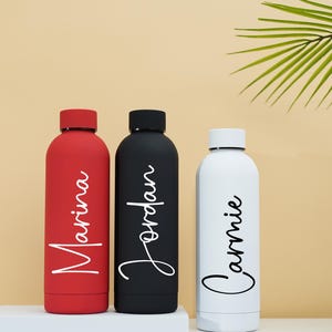 May include: Three stainless steel water bottles with personalized names: Marina, Jordan, and Cammie. The bottles are red, black, and white.