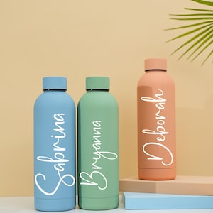 May include: Three personalized water bottles in blue, green, and peach colors. The bottles are labeled with the names Sabrina, Bryanna, and Deborah.