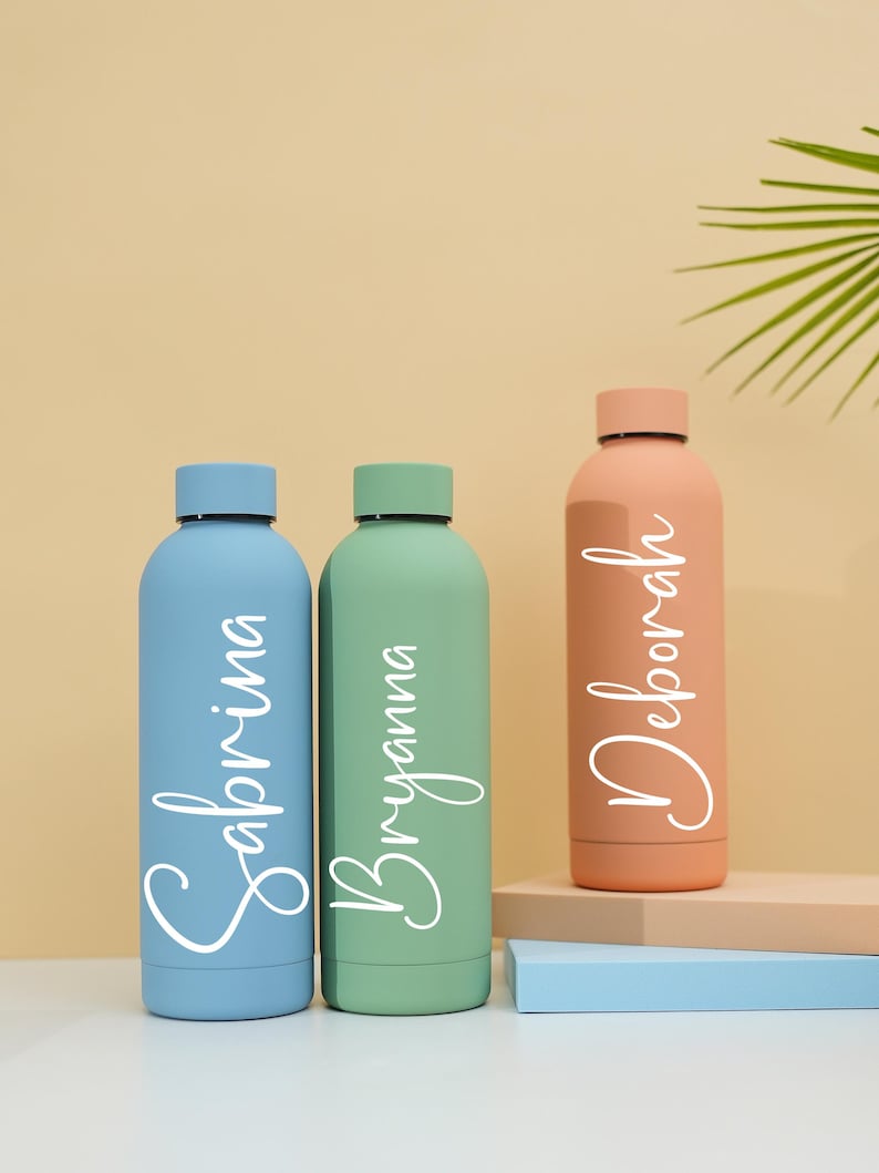 May include: Three personalized water bottles in blue, green, and peach colors. The bottles are labeled with the names Sabrina, Bryanna, and Deborah.