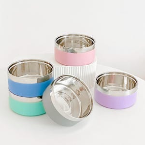 May include: A collection of stainless steel pet bowls with colorful silicone bases. The bowls are in various colors, including pink, blue, green, gray, and purple. The bowls have a shiny, metallic interior and a smooth, matte exterior.