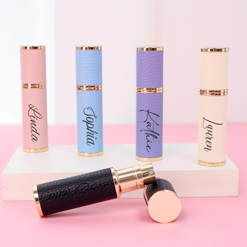 May include: A collection of refillable perfume atomizers in various pastel colors, including pink, blue, and lavender. Each atomizer has a gold-colored top and bottom, with a textured leather-like finish. Names are printed on the atomizers.