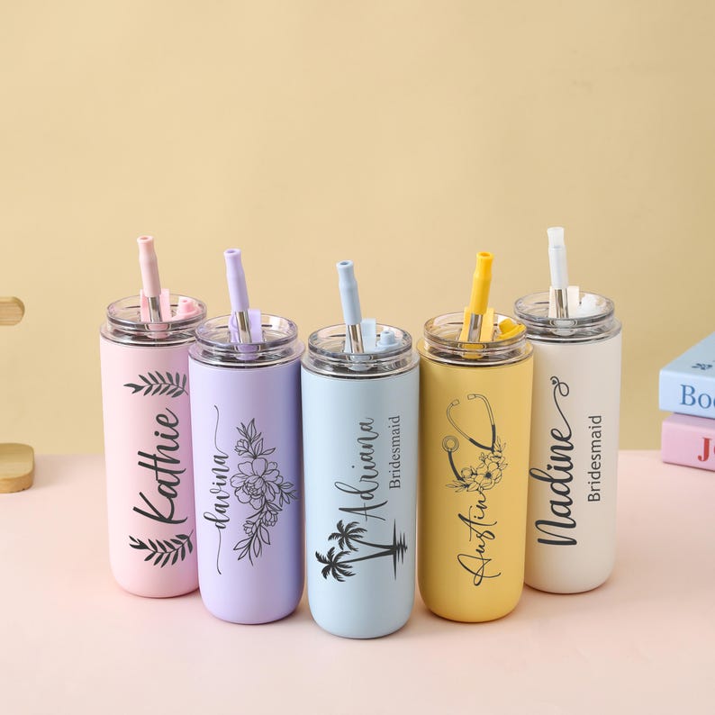 May include: Five personalized stainless steel tumblers with straws in pastel colors: pink, lavender, light blue, yellow, and white. Each tumbler features a name and a decorative design, such as leaves, flowers, or a stethoscope.