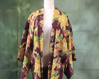 May include: A burgundy kimono-style jacket with a floral pattern in yellow, orange, and green. The jacket is displayed on a mannequin, showcasing its open front and wide sleeves. The floral design is detailed with white outlines.