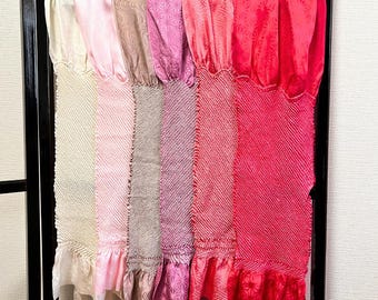 May include: A display of colorful, patterned fabric panels in shades of cream, pink, and red. Each panel has a ruffled edge. The fabrics are hanging on a black metal frame.