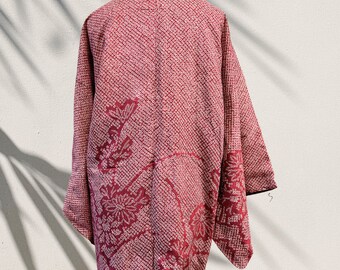 May include: A red and white haori jacket featuring a dense shibori-style tie-dye pattern of small circles. The garment displays larger floral motifs integrated into the textured fabric, with wide sleeves and a structured collar design.