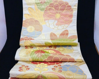 May include: A white fabric with a floral pattern in shades of gold, pink, green, and blue. The fabric is folded in a stack, showing the pattern on each layer.