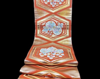 May include: A folded orange and gold textile with a repeating pattern of hexagonal shapes and diamond accents. Each hexagon features a floral design in shades of blue and white. The fabric's layered construction is visible at the bottom.