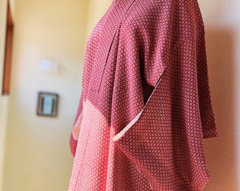 May include: A red and white patterned kimono displayed on a mannequin. The kimono features a small, repeating square pattern in red and white. The garment has wide sleeves and a wrap-around design, showcasing traditional Japanese attire.
