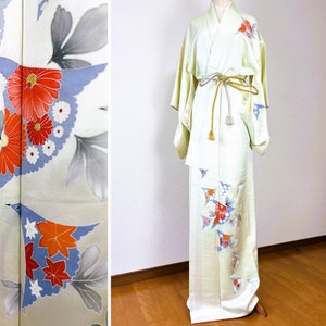 以下が含まれることがあります： 赤、オレンジ、青の花と葉の模様が入った薄緑色の着物。着物は金と銀の帯で結ばれています。マネキンに着物が飾られています。