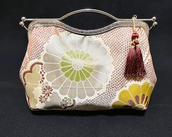 May include: A small, cream-coloured clutch bag with a silver metal frame and a burgundy tassel. The bag features a floral pattern with red, green, and gold accents.