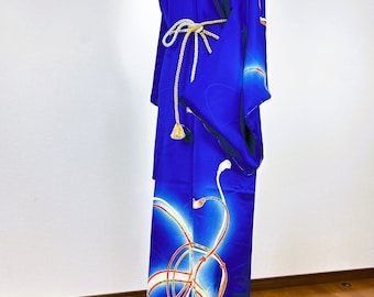 Puede incluir: Un kimono azul vibrante con un patrón abstracto y fluido de líneas curvas blancas y naranjas. La prenda se sujeta a la cintura con un cordón trenzado blanco y dorado, atado en un nudo con borlas colgantes en los extremos.