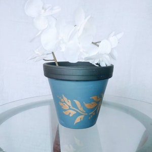 May include: A blue ceramic planter with a gold leaf design, holding a white silk orchid.