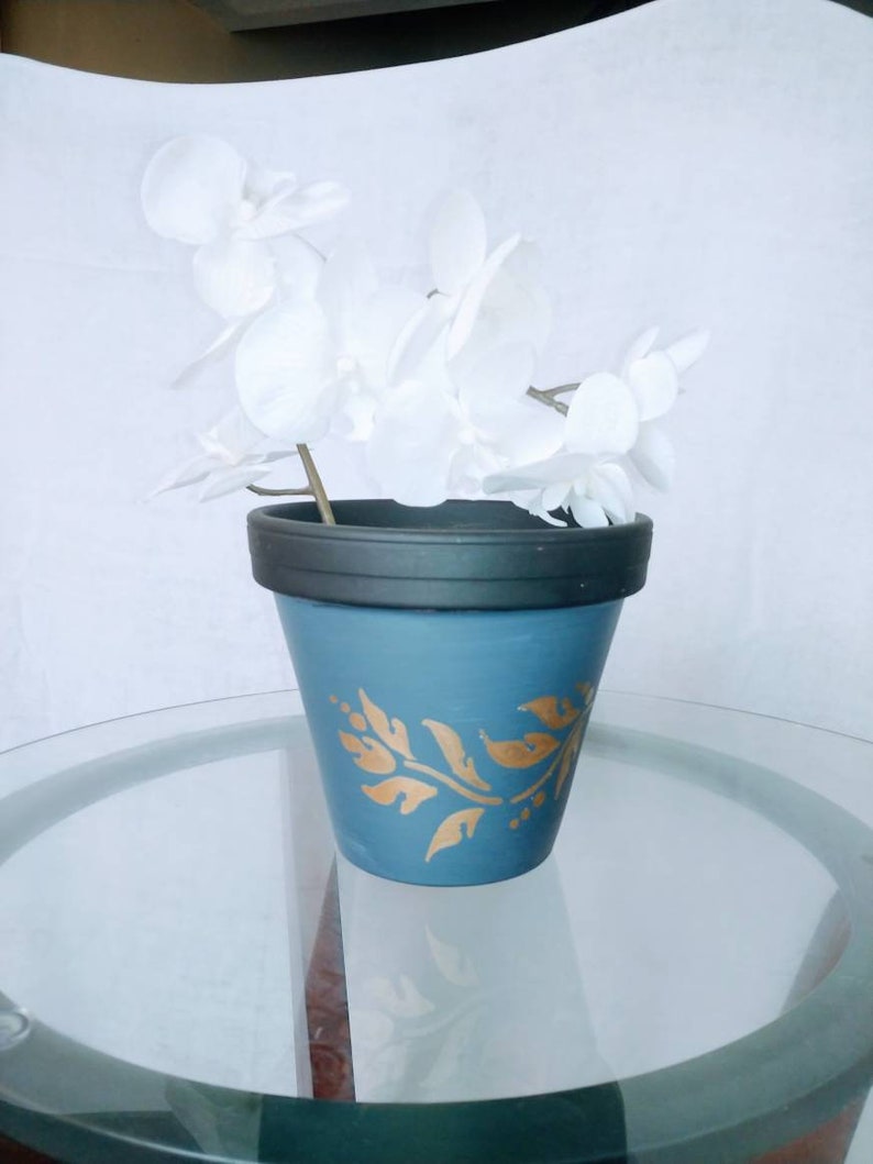 May include: A blue ceramic planter with a gold leaf design, holding a white silk orchid.