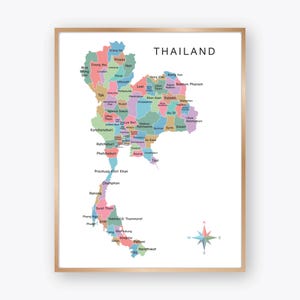 May include: A framed map of Thailand, showing the provinces in various colours. The word "THAILAND" is printed in black at the top. A compass rose is in the lower right corner. The frame is a light brown colour.